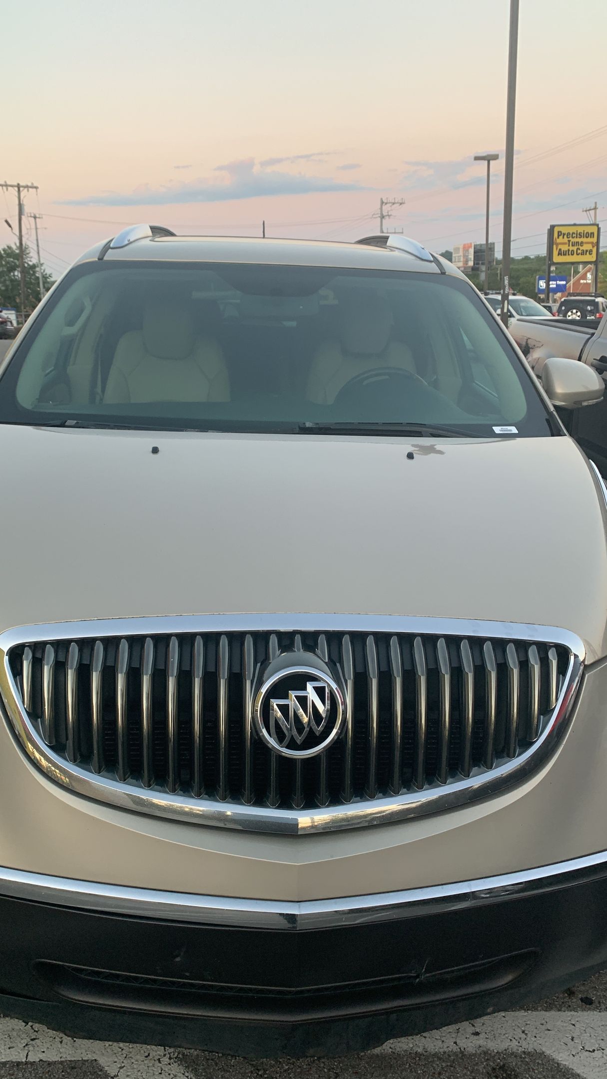 Front view of a white Buick SUV parked outdoors at dusk, with a dealership lot in the background