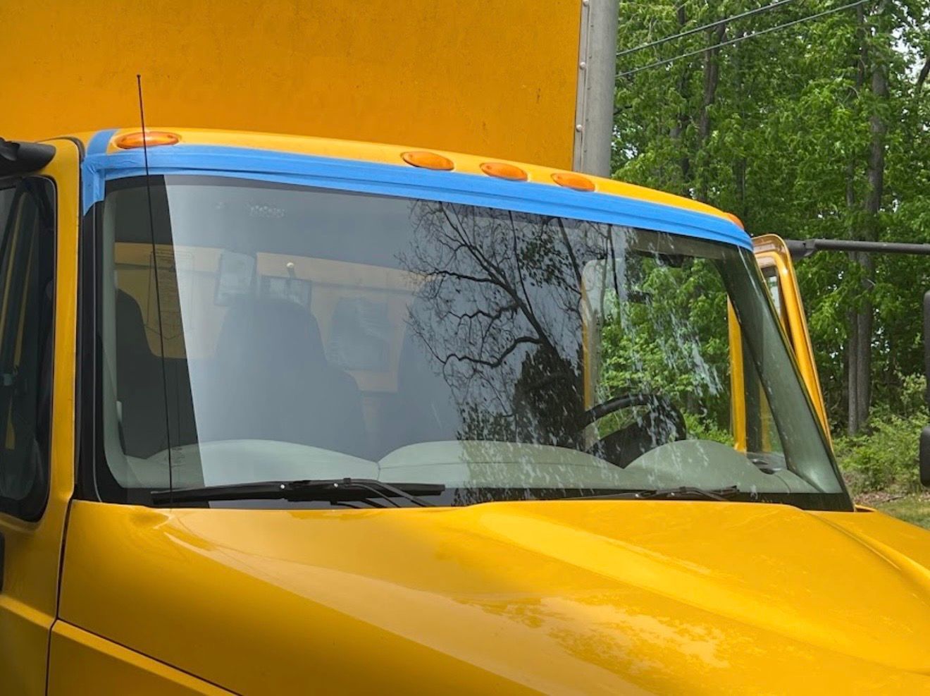 Yellow truck cab with blue roof and windshield, parked outdoors near green trees