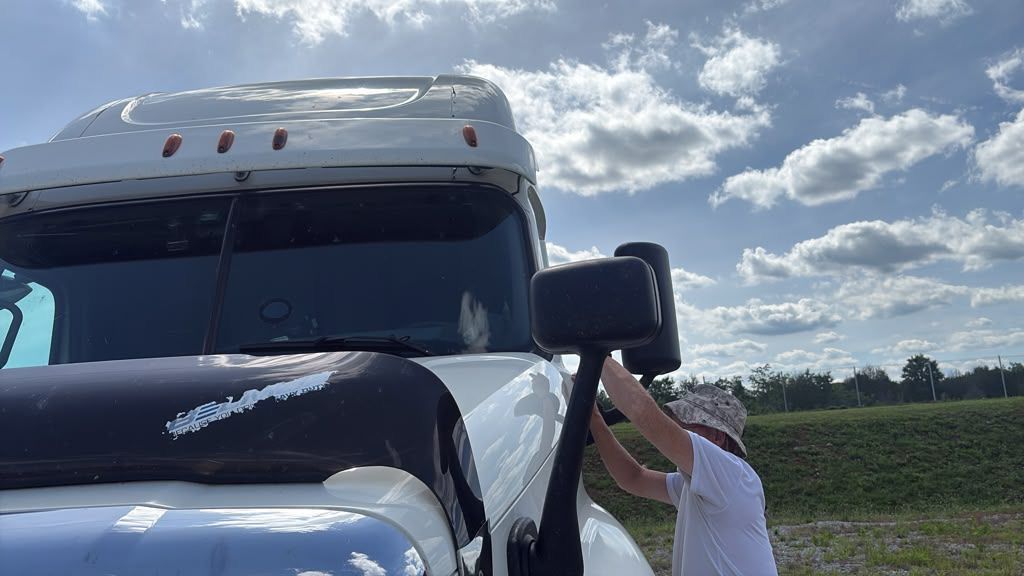 Person opening the door of a white truck in a rural field under a cloudy sky