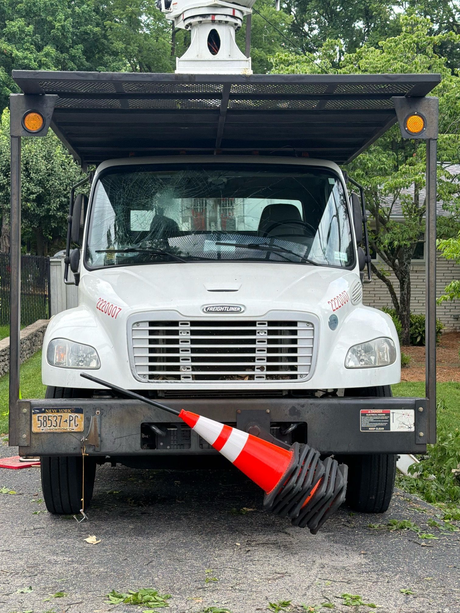White utility truck with a raised black canopy and an orange traffic cone caught under the front bumper.