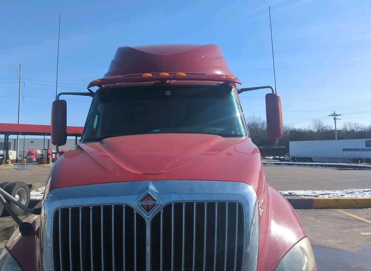 Red semi-truck parked outdoors in a snowy lot, front view with chrome grille and cab visor.